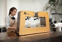 a woman in an apron is standing in front of a coffee machine